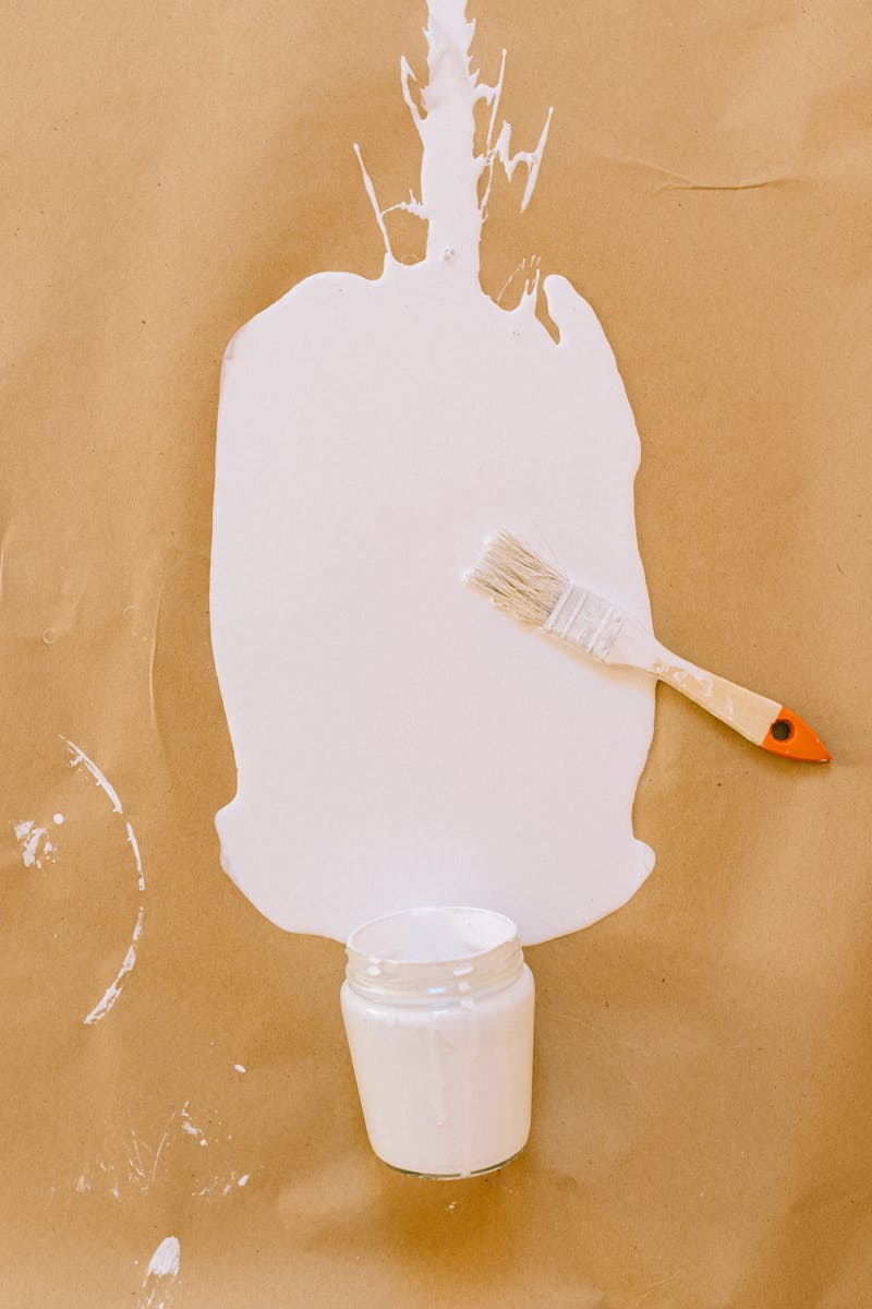 A brush beside a white paint spill on brown paper, showcasing a creative art setup.