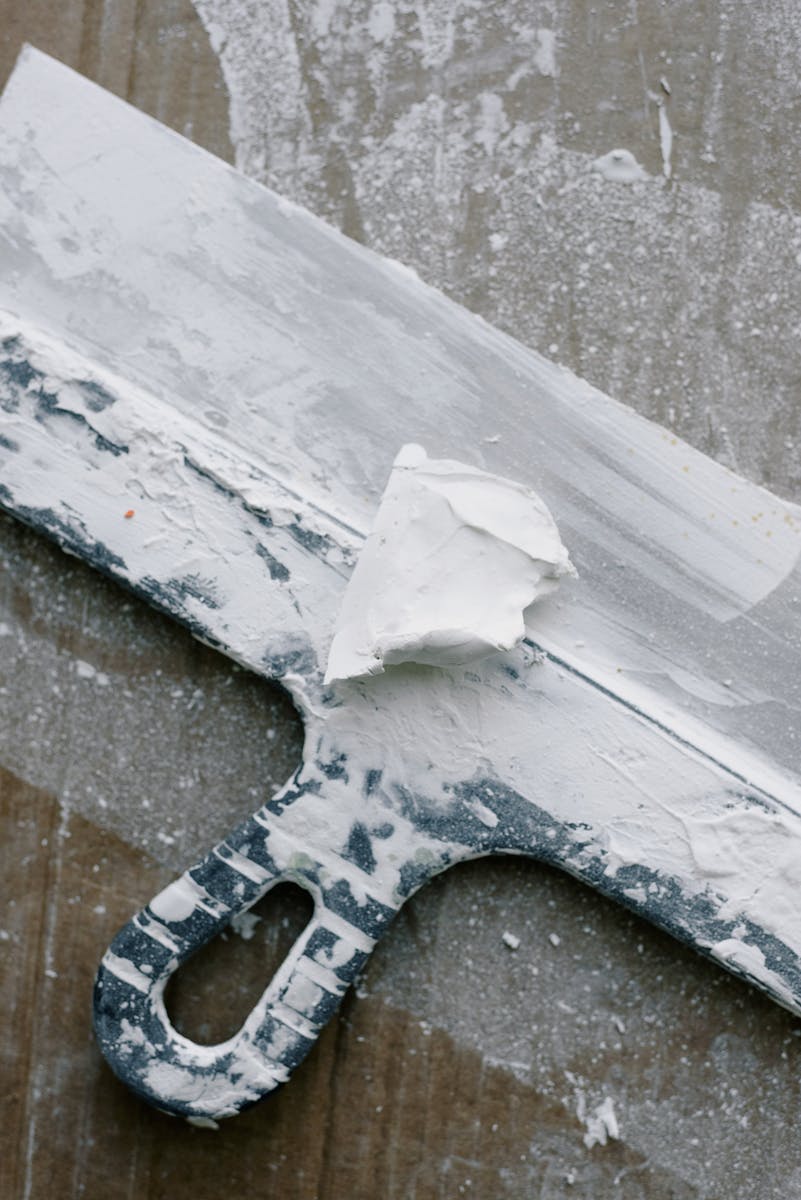 From above of spatula in dust and plaster on wooden table during renovation